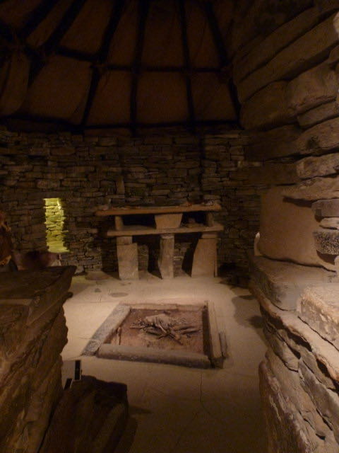 Wnętrze kamiennego domu w Skara Brae: kamienny kredens, kamienne łóżka i palenisko pośrodku