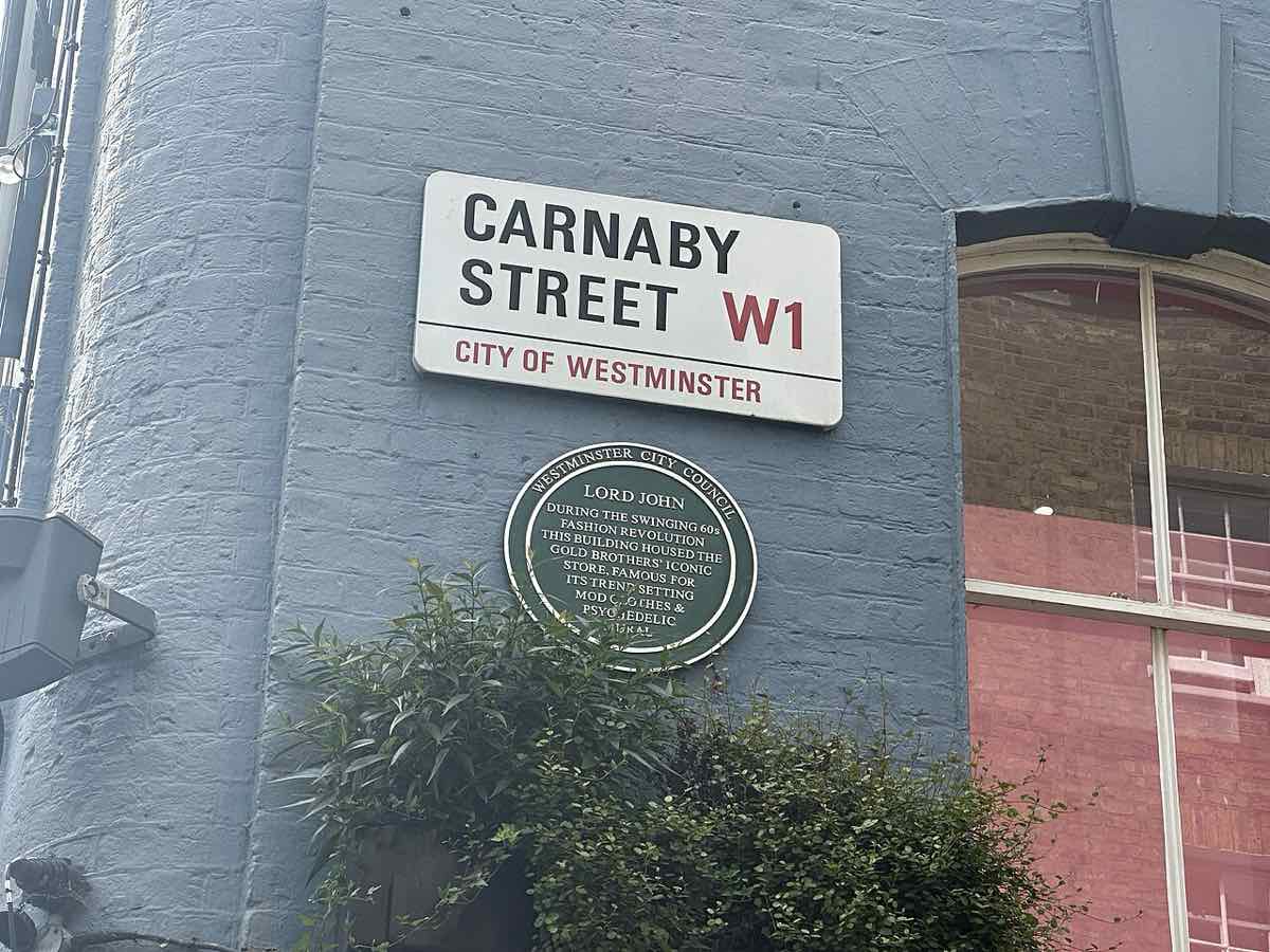 Tabliczka z nazwą ulicy Carnaby Street w Londynie, a pod nią zielona tablica pamiątkowa o sklepie z modą z lat 60.